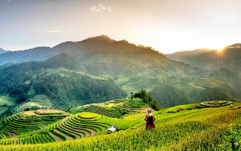 Sunrise over the Mu Cang Chai rice terraces with a woman in traditional dress on the hillside